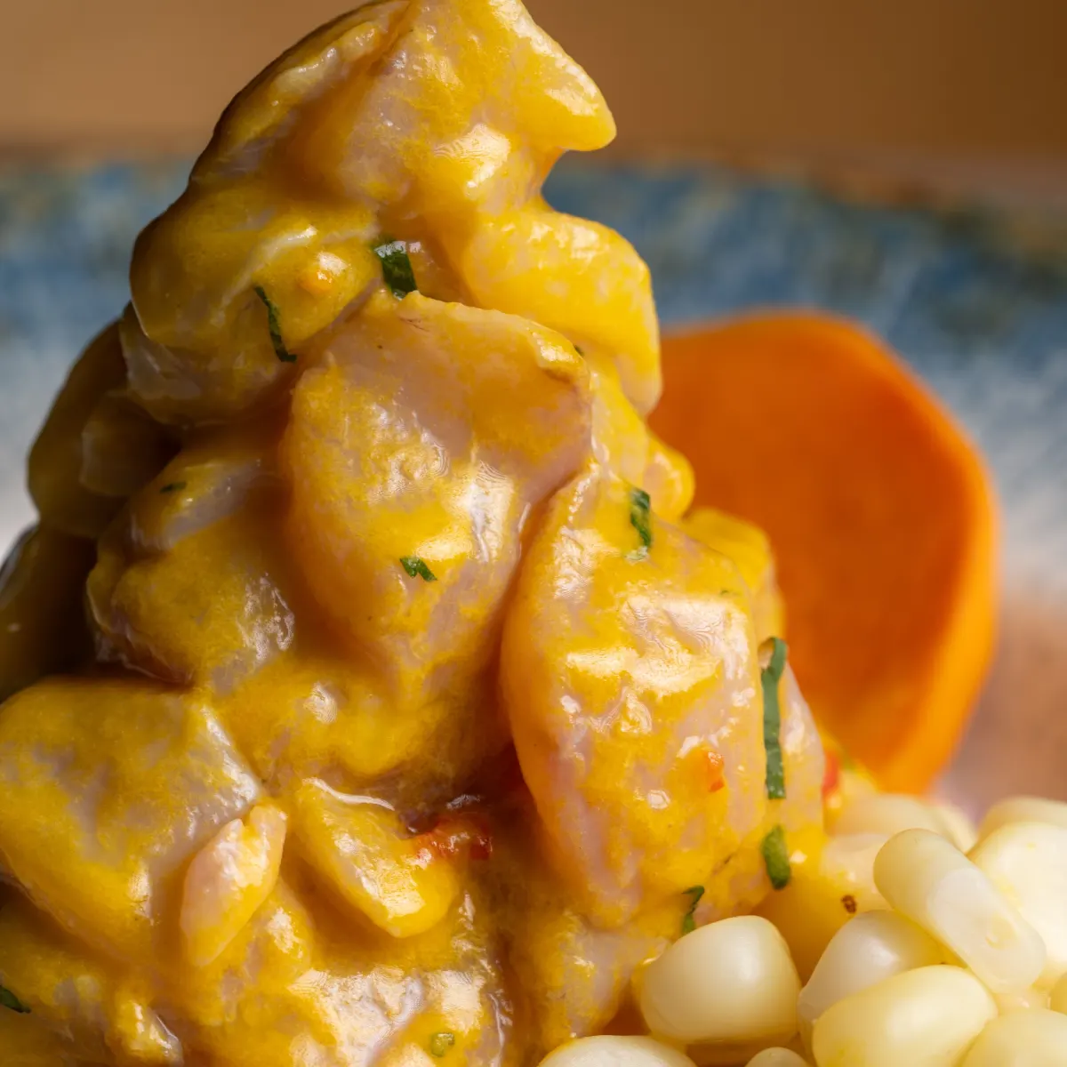 Cubos de pescado bañados en leche de tigre de ají amarillo, con granos de choclo y una rodaja de camote