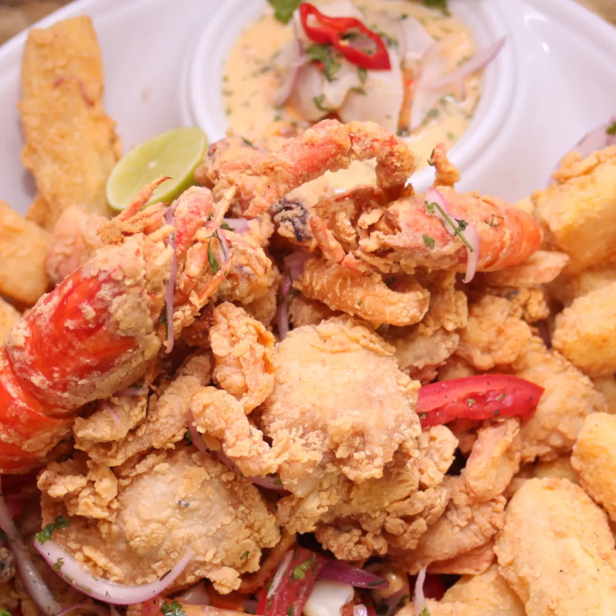Pescado y mariscos apanados y fritos con yuca, sarza criolla y medio limón en un plato blanco