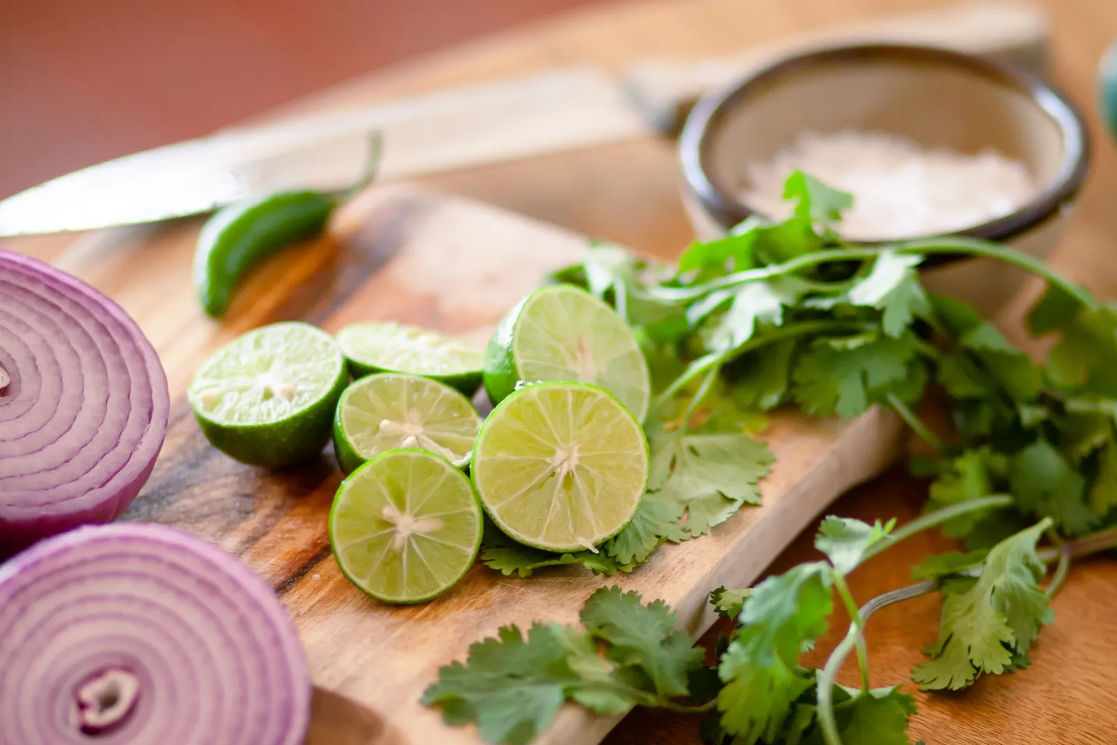 Limones partidos, cebolla morada, ají verde y cilantro sobre una tabla de madera