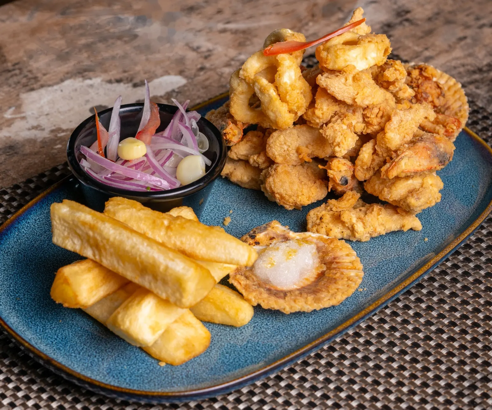 Fuente de chicharrón crocante con bastones de yuca frita y sarza criolla sobre una bandeja azul